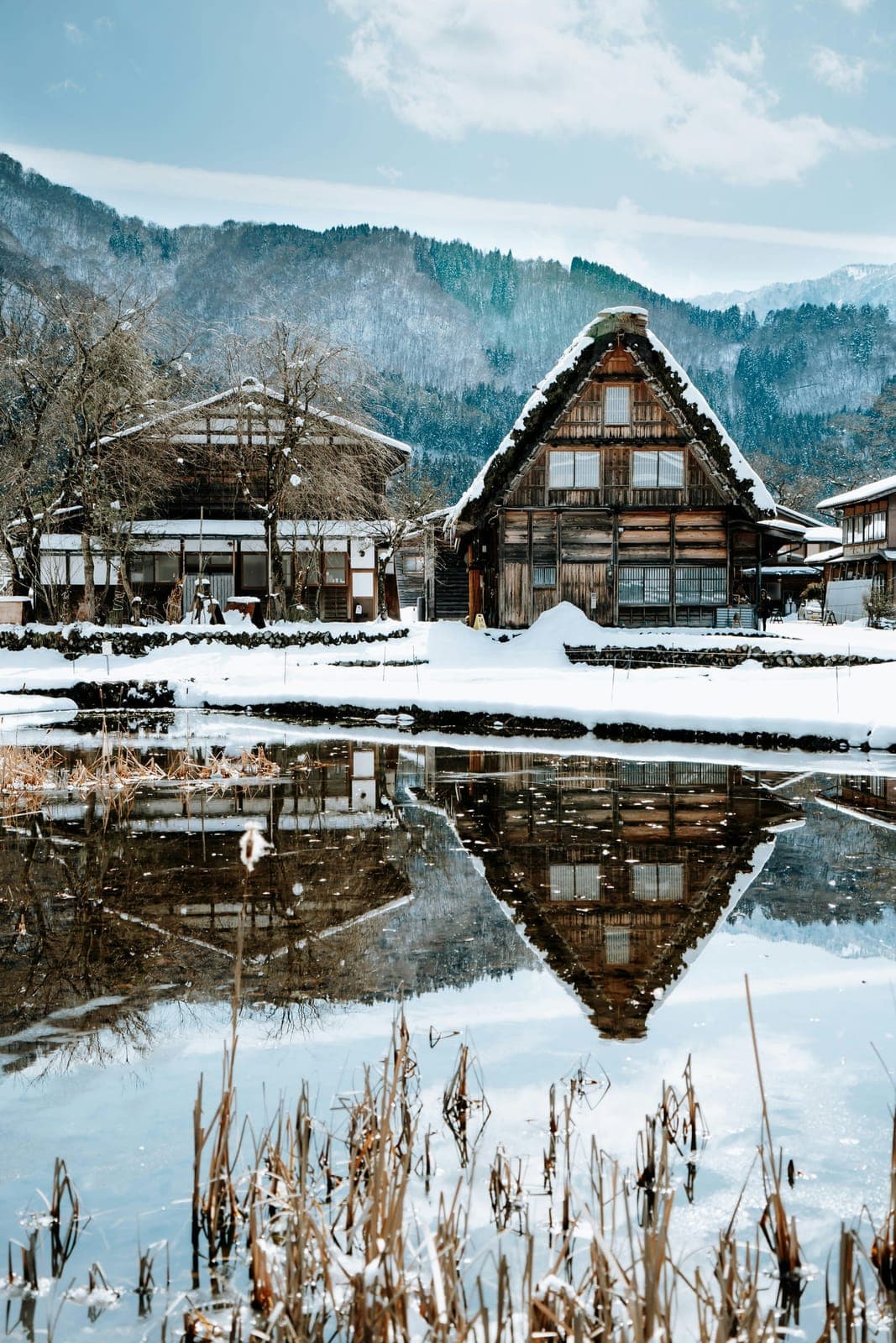 岐阜・雪の白川郷で、水面に映る合掌造りの茅葺き家屋